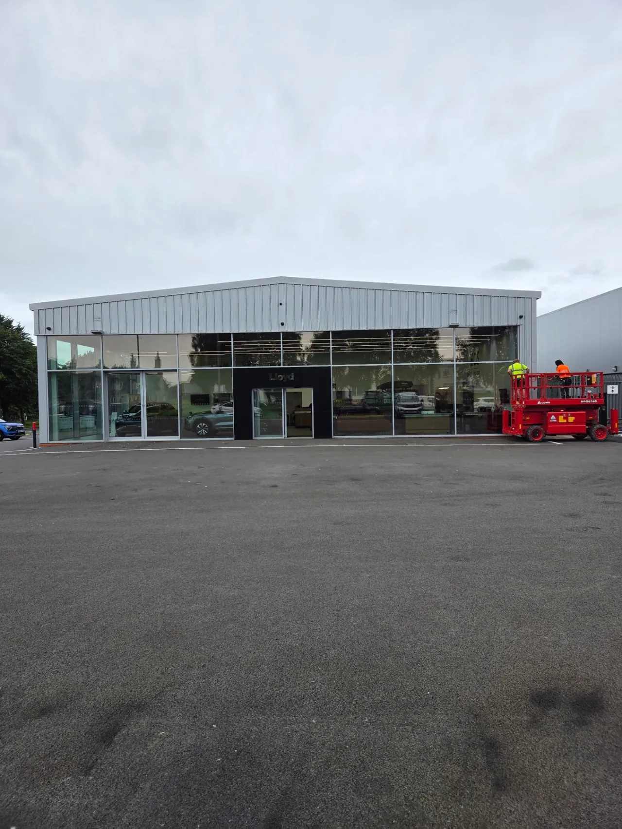 Company-supplied photograph: Original light grey showroom frontage with scissor lift on site