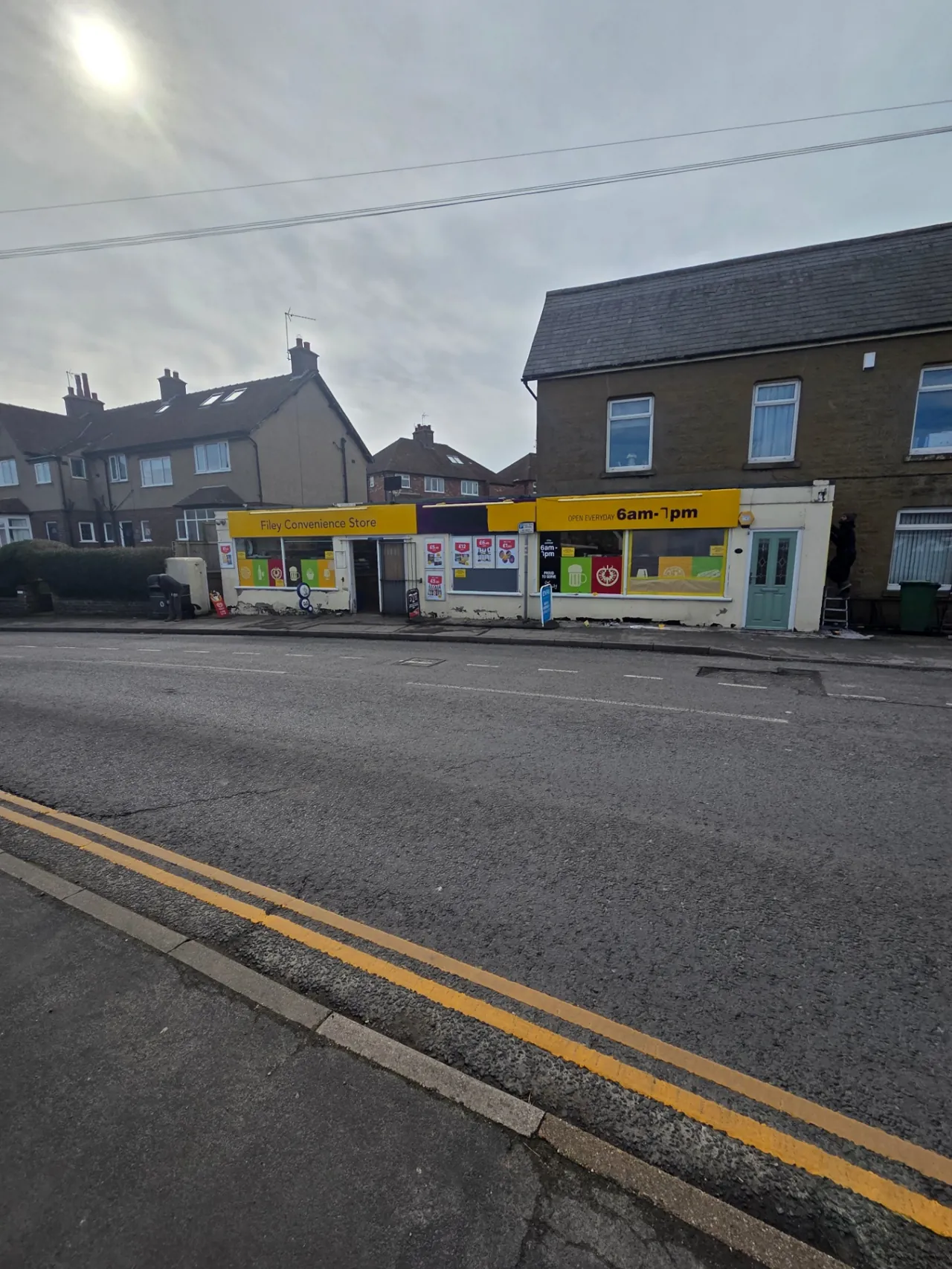 Company-supplied photograph: Company-supplied photograph of Filey Convenience Store before respraying, with the weathered cream shopfront and yellow fascia