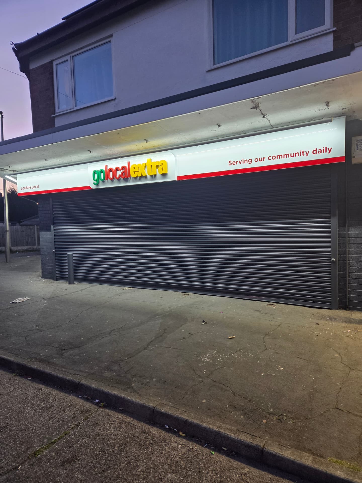 Company-supplied photograph of a resprayed Go Local store roller shutter and fascia at night
