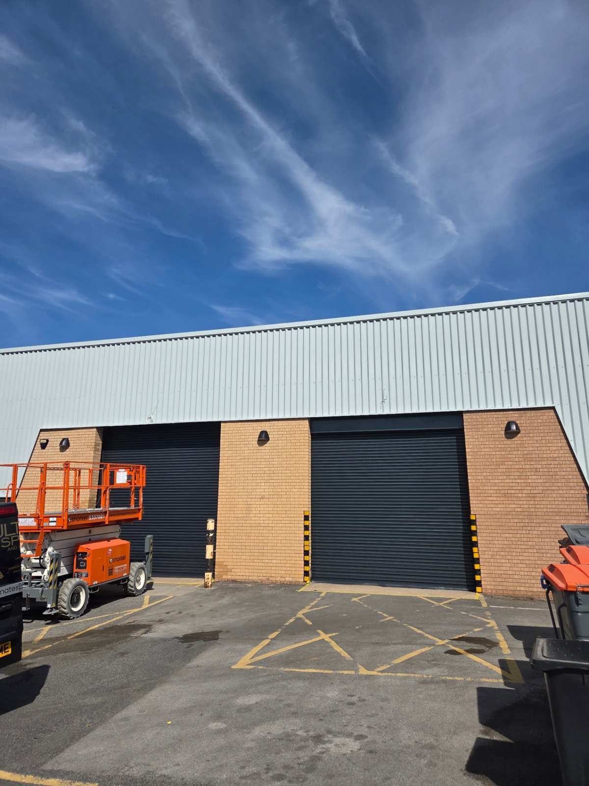 Company-supplied photograph: Bradford loading bays with RAL 7016 anthracite grey roller shutters beneath RAL 7035 light grey cladding