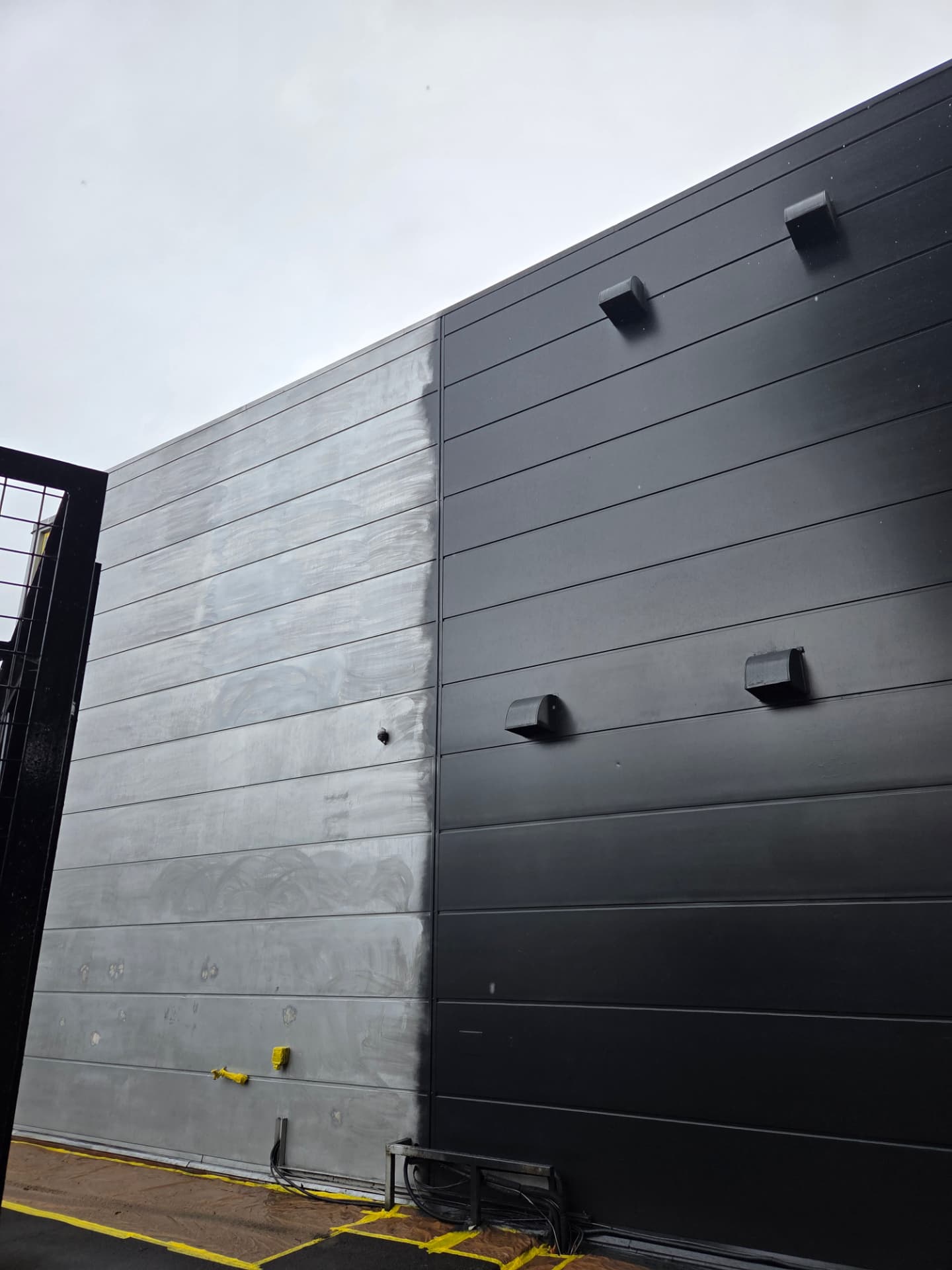 Company-supplied photograph of the showroom wall with resprayed black cladding beside the original grey panels