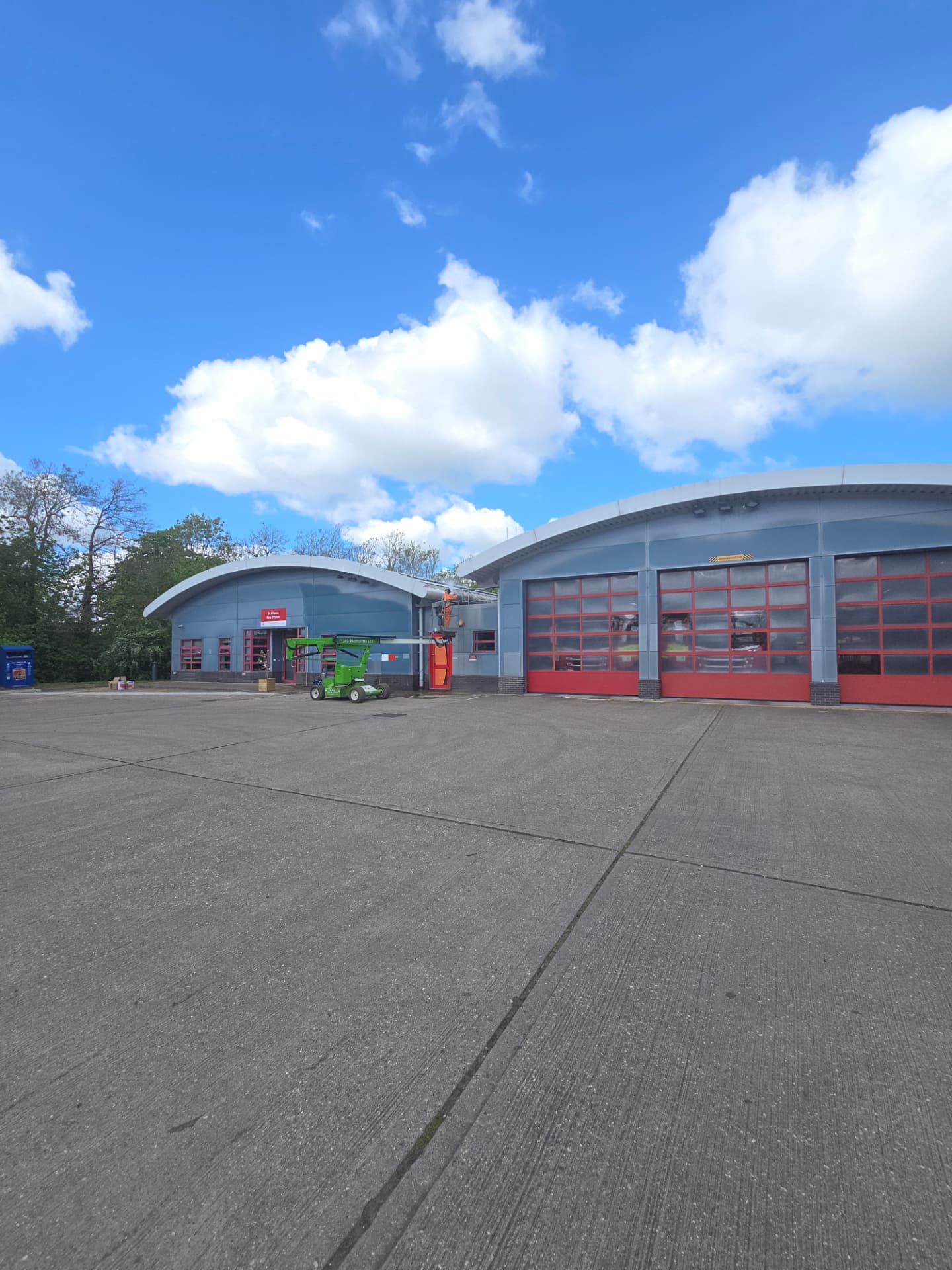 Company-supplied photograph of the fire station across the yard with original grey panels and access equipment in place