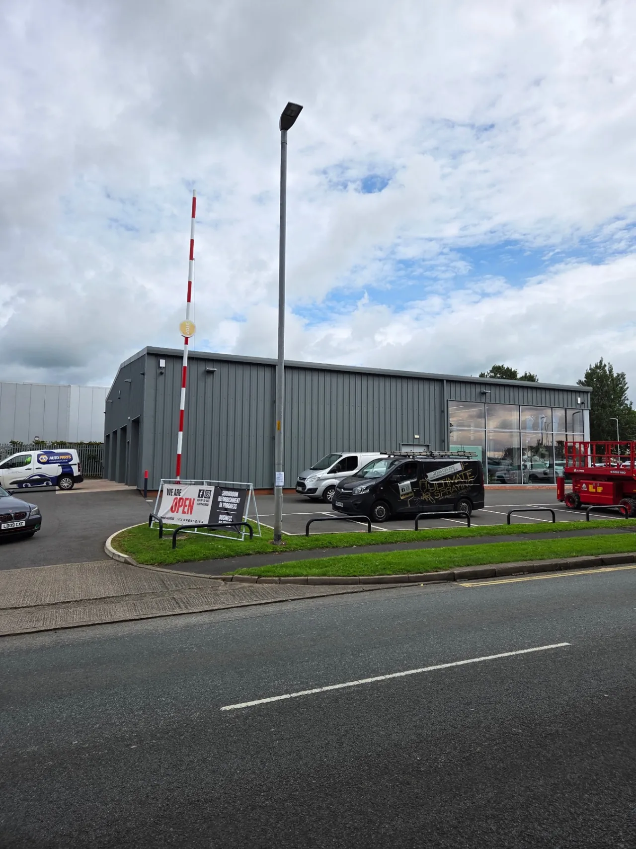 Company-supplied photograph: Completed showroom exterior with Ultimate Spraying vehicle and scissor lift on site
