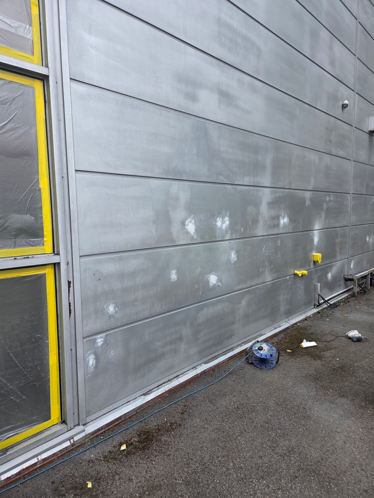 Company-supplied photograph: Company-supplied photograph of the CD Bathrooms showroom cladding before respraying, with original grey panels, filled and repaired holes and masking in place