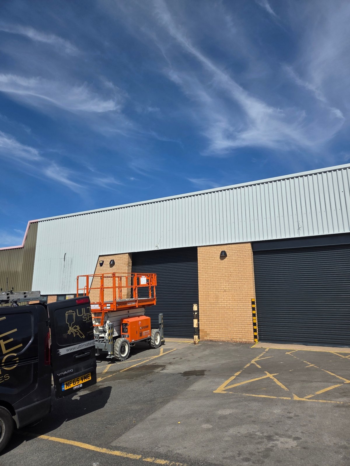 Company-supplied photograph: Scissor lift beside resprayed Bradford loading bays with light grey cladding and anthracite grey shutters