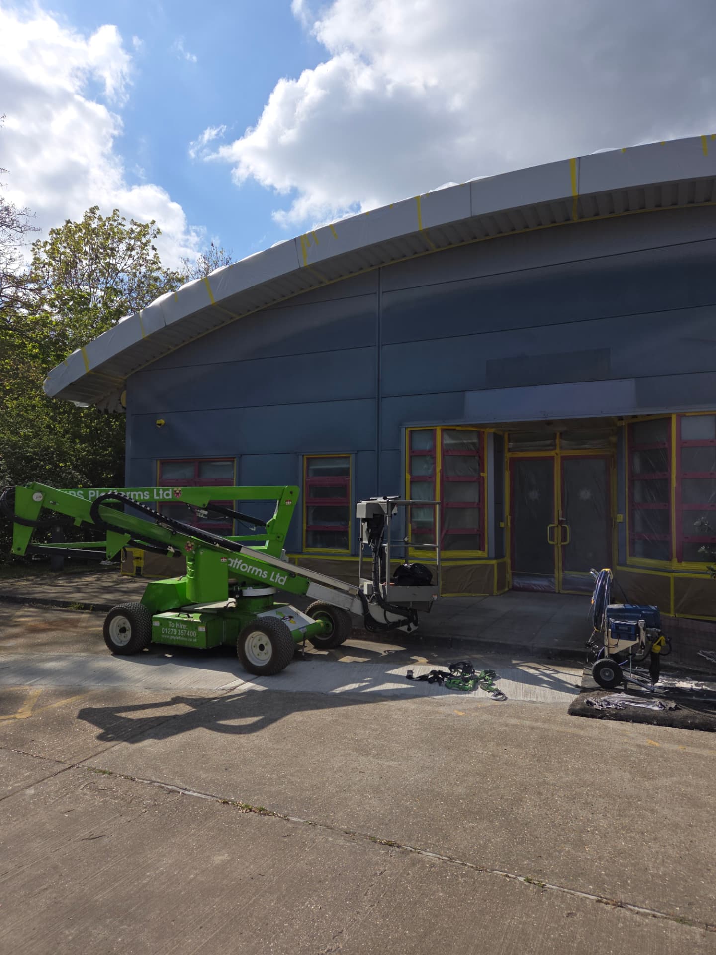 Company-supplied photograph of the fire station entrance elevation masked for respraying, with a boom lift and access platform in place
