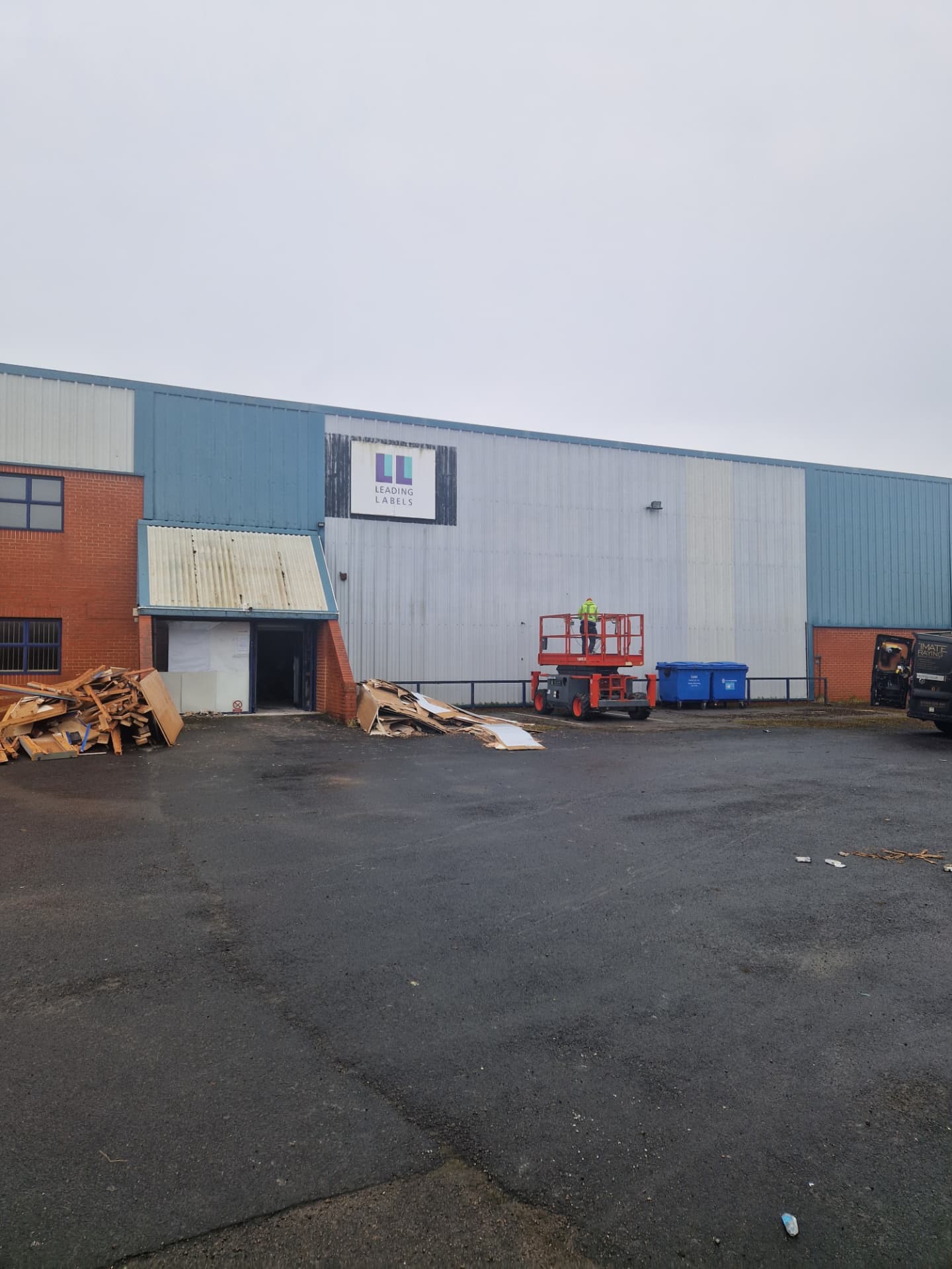 Company-supplied photograph: X Martial Arts building in York before respraying, with original blue and grey cladding and a scissor lift on site