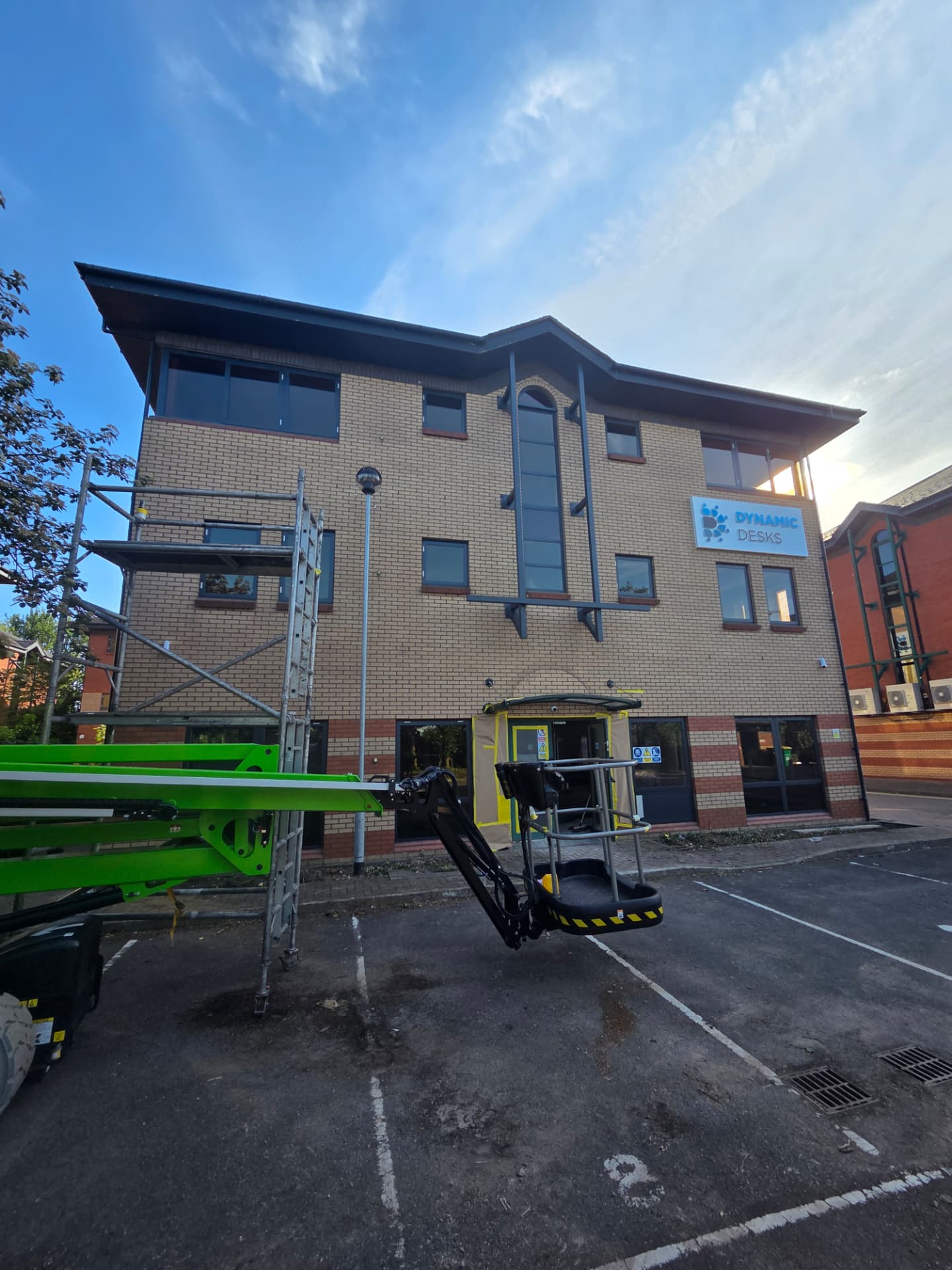 Company-supplied photograph of Dynamic Desks front-elevation windows with boom lift and access tower, and entrance masking still in place